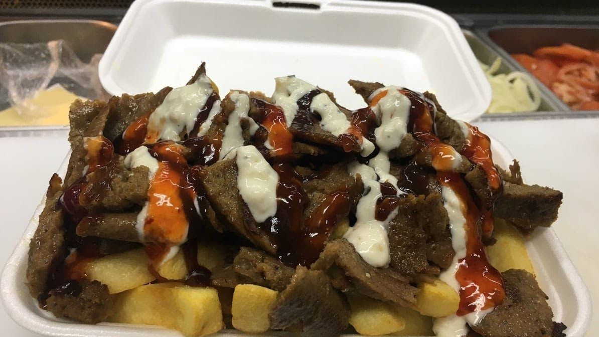 Lamb kebab meat on chips with garlic, BBQ and chilli sauce in styrofoam container