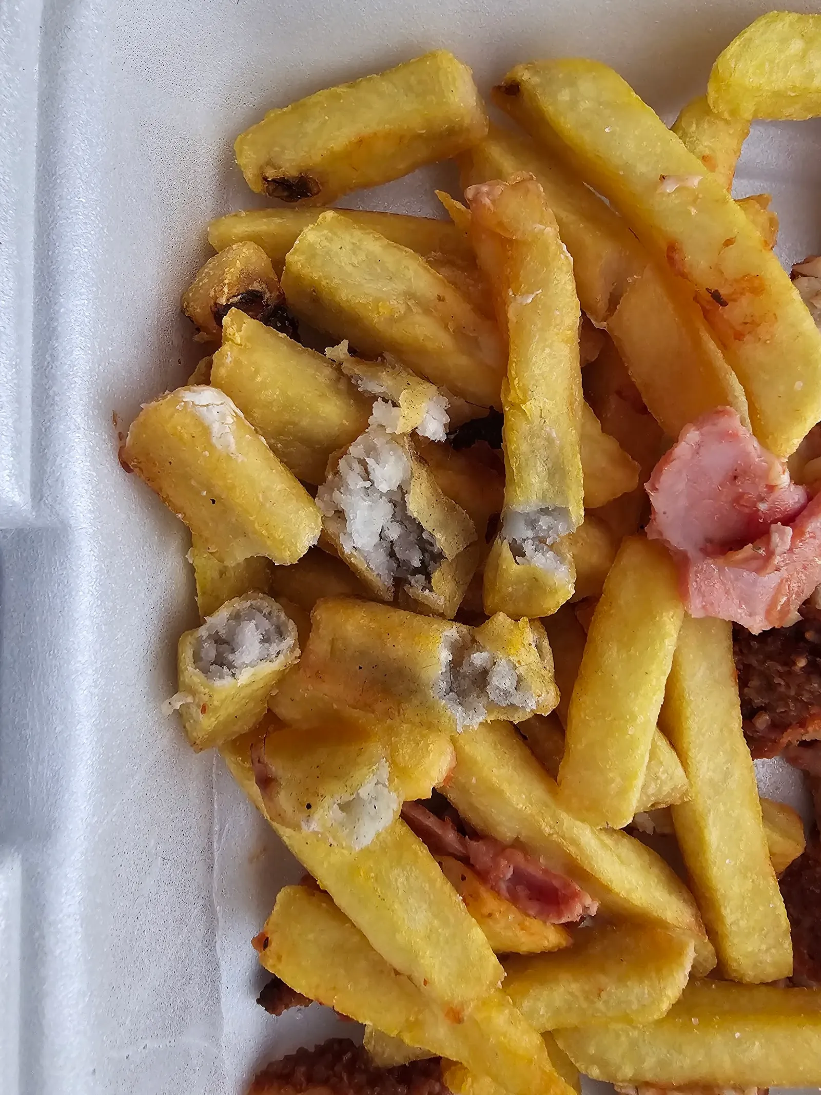 Chips and cut-open dim sims in a styrofoam takeaway container