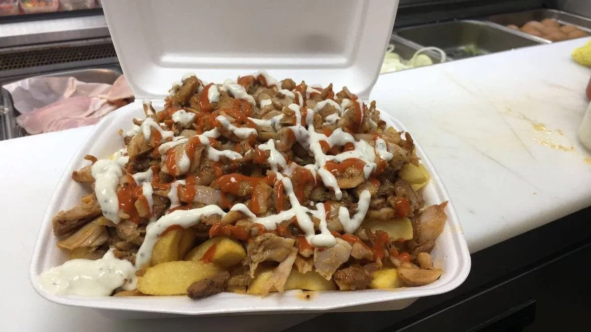 Chicken kebab meat on chips with chilli and garlic sauce in open styrofoam container
