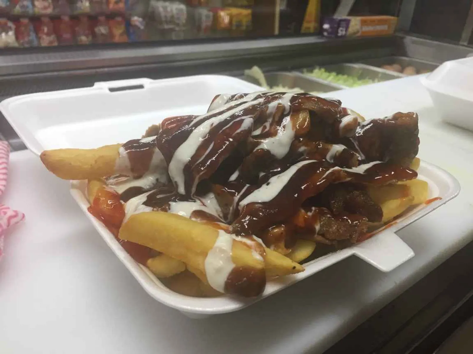 Chips loaded with meat and mixed sauces in a styrofoam container on prep counter
