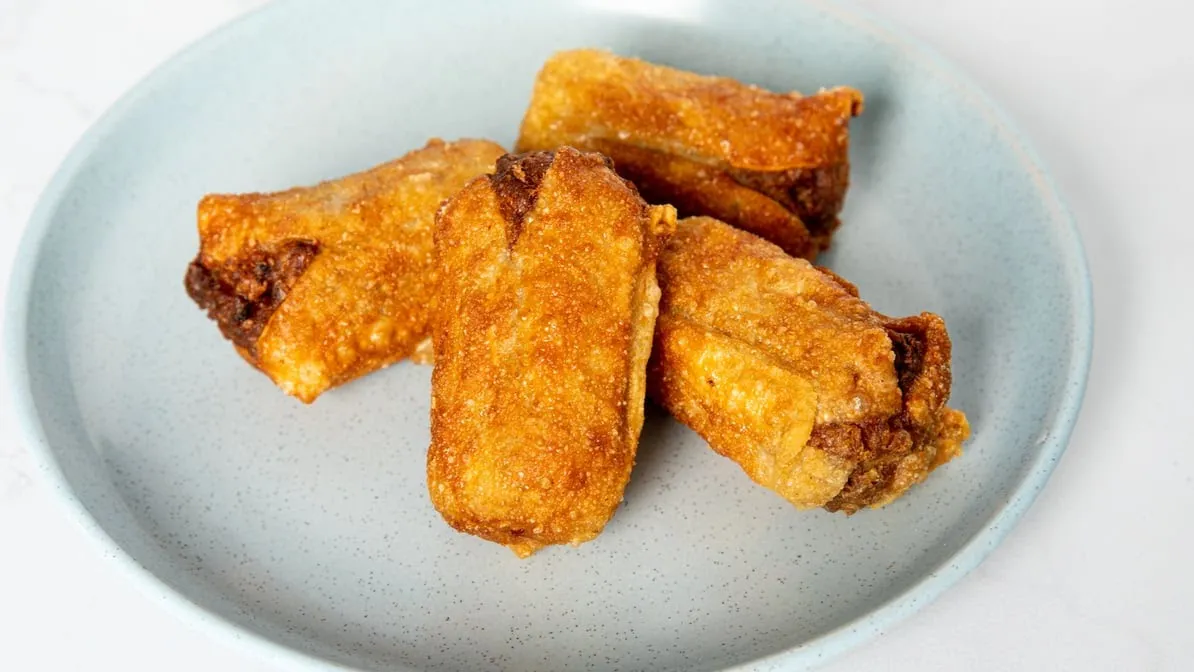 Four golden fried dim sims on a grey ceramic plate, studio photo