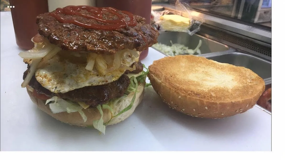 Open double beef burger with egg and lettuce on prep surface, bun aside