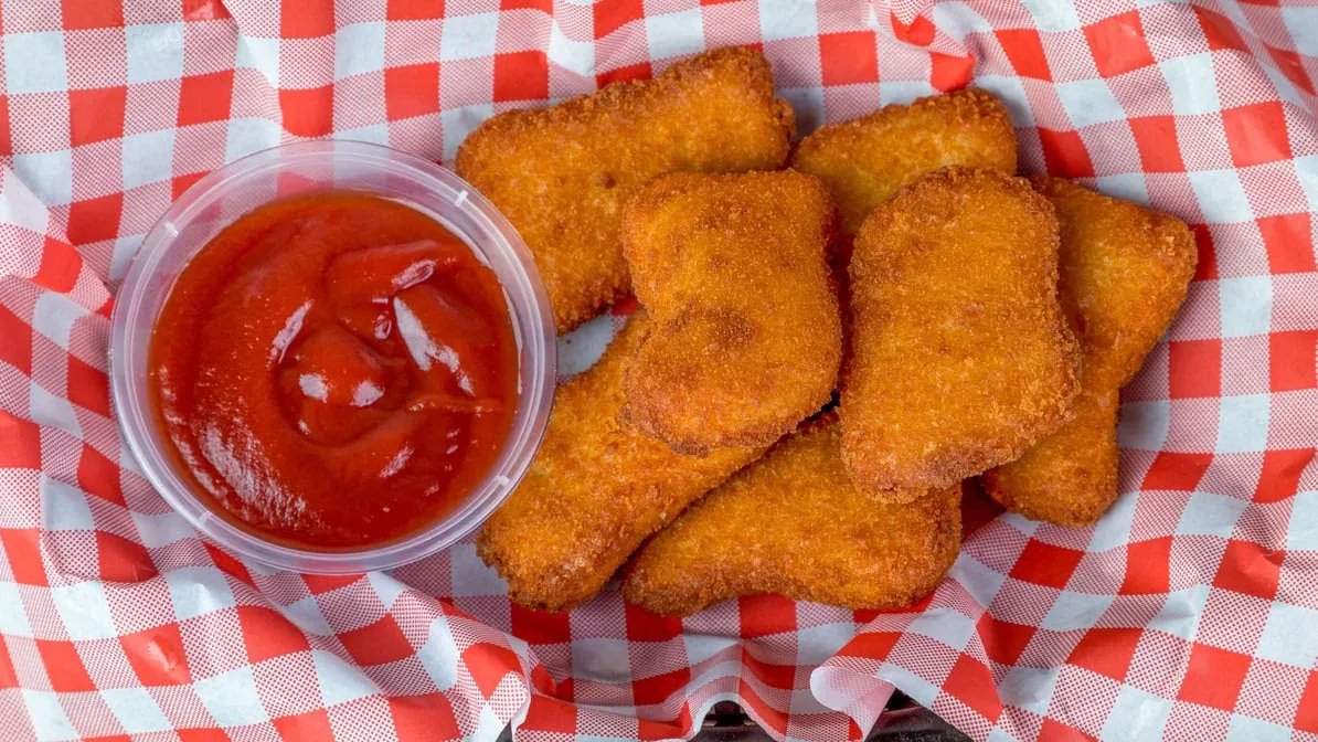 Crumbed chicken nuggets in a checkered basket with tomato sauce
