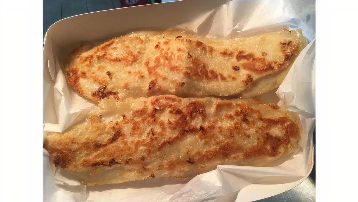 Two golden cheese calzones or cheese scrolls in a paper-lined takeaway tray
